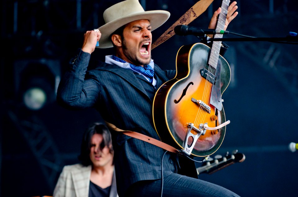 Man In Black Formal Suit Holding Electric Guitar While Raising His Right Hand And Opening His Mouth In Tilt Shift Lens Photography