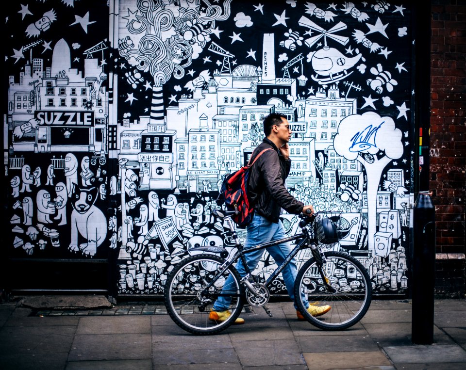 Man In Black Jacket Holding A Black Hardtail Bike Near Black And White Art Wall