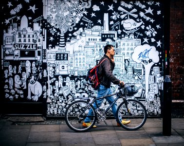 Man In Black Jacket Holding A Black Hardtail Bike Near Black And White Art Wall photo