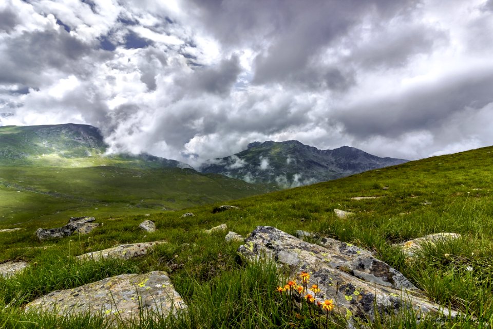 Green Grass Field With Rocks Near Mountains During Cloudy Daytime Sky photo