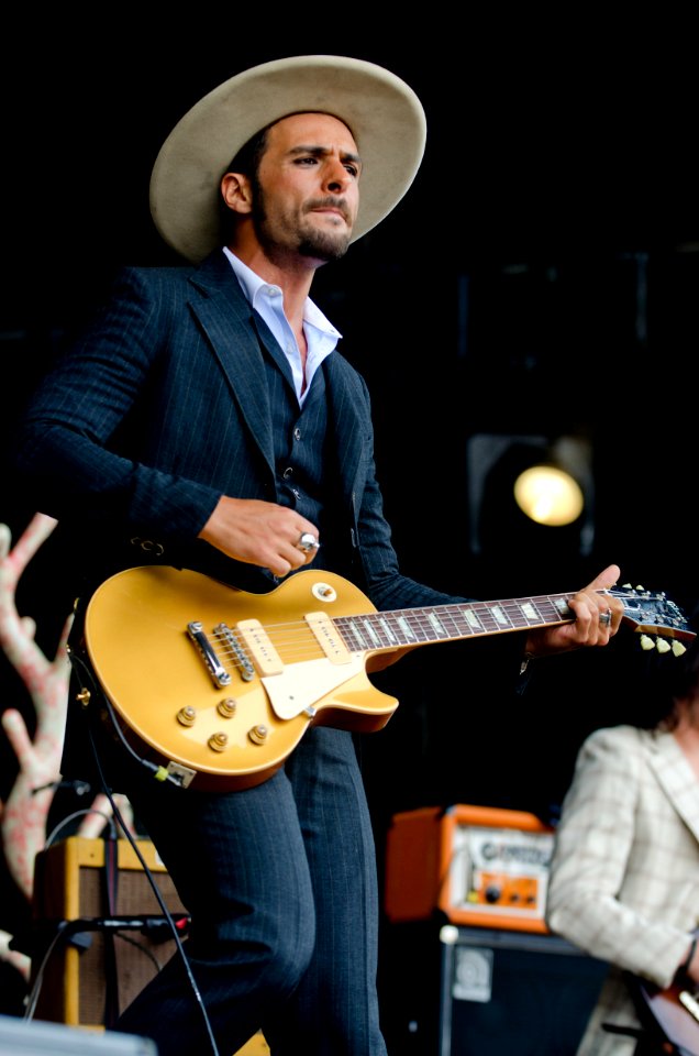 Man In Black And White Pinstripe Formal Coat And Pants Wearing Beige Hat Holding Brown Electric Guitar