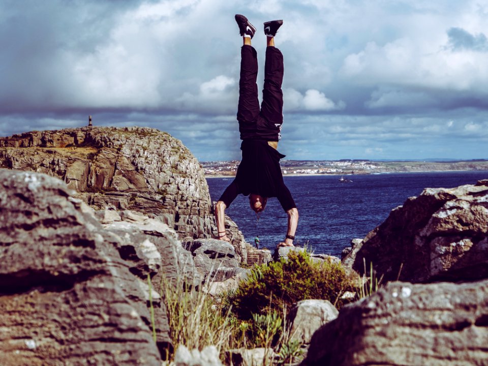 Man Wearing Black Dress Shirt And Burgundy Pants Hand Standing On Rock Formations Across Sea