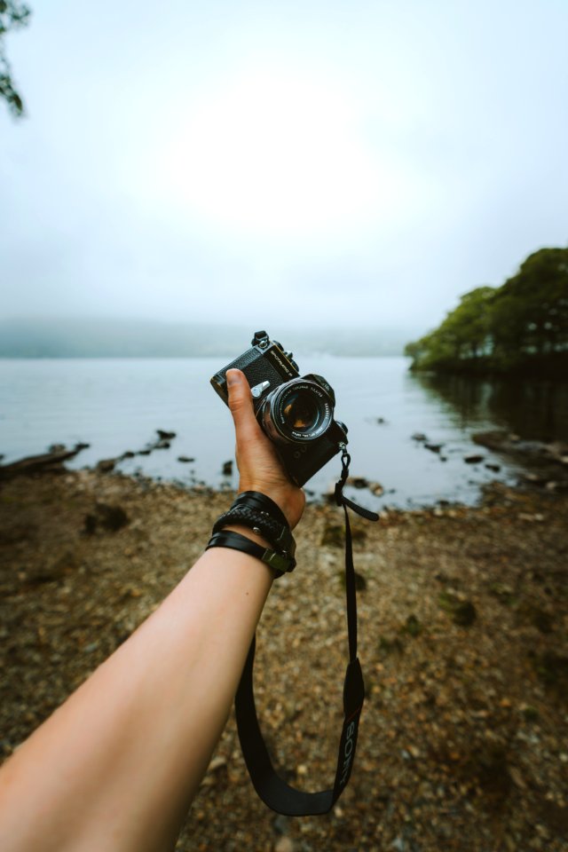 Person Holding Black Camera Front Body Of Water