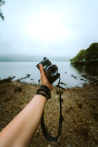 Person Holding Black Camera Front Body Of Water
