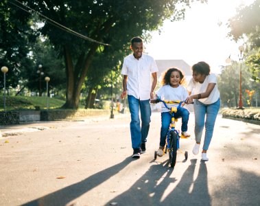 Man Standing Beside His Wife Teaching Their Child How To Ride Bicycle photo