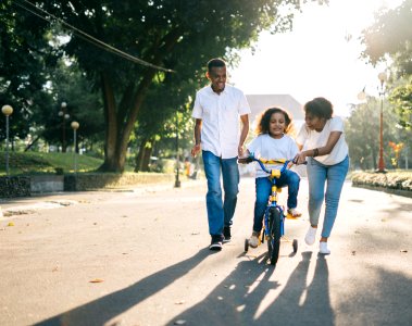 Man Standing Beside His Wife Teaching Their Child How To Ride Bicycle