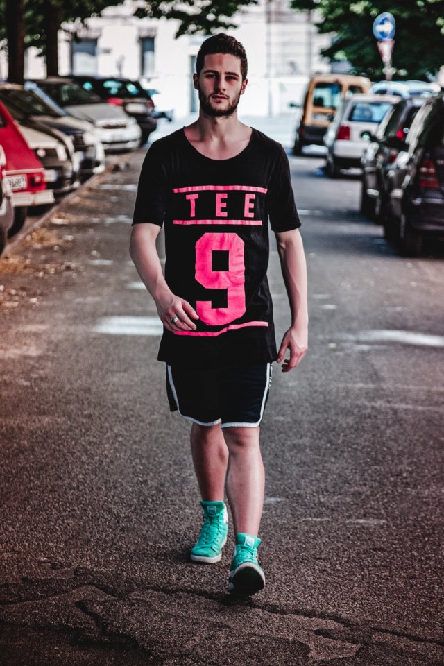 Man Wearing Black Crew-neck T-shirt Black Shorts And Pair Of Teal High-top Sneakers Walking Between Vehicles