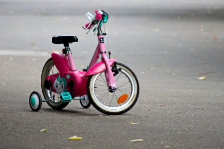 Pink Bike With Training Wheels On Gray Pave Road
