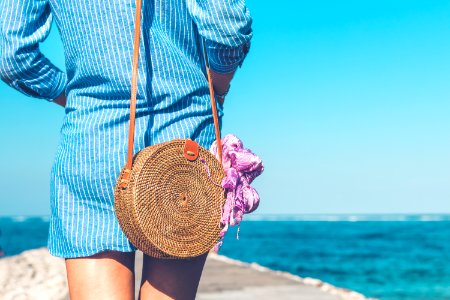 Woman Wearing Blue And White Striped Dress With Brown Rattan Crossbody Bag Near Ocean