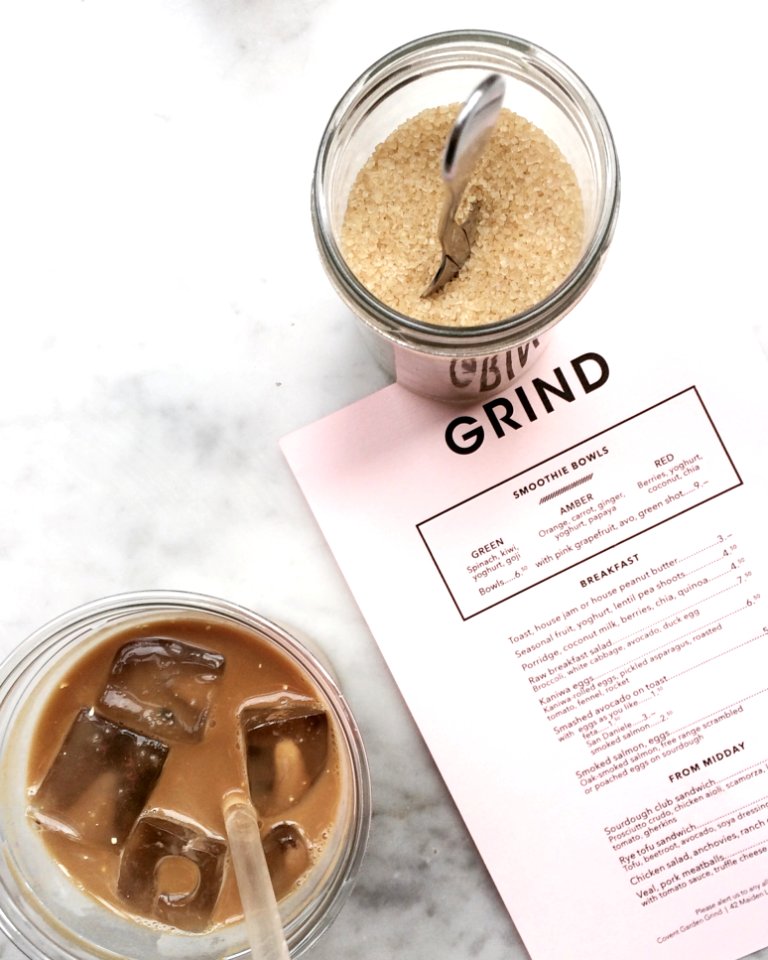 Clear Drinking Glass Filled With Tea And Ice Cubes With Clear Plastic Straw Beside Clear Glass Canister Filled With Brown Sugar