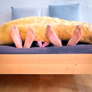 Family Of Three Lying On Bed Showing Feet While Covered With Yellow Blanket