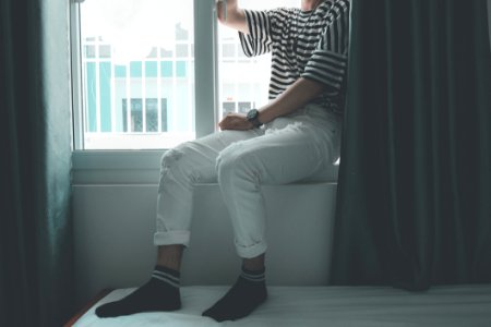 Woman Sitting On Window Stepping On White Bed Inside Well Lighted Room photo