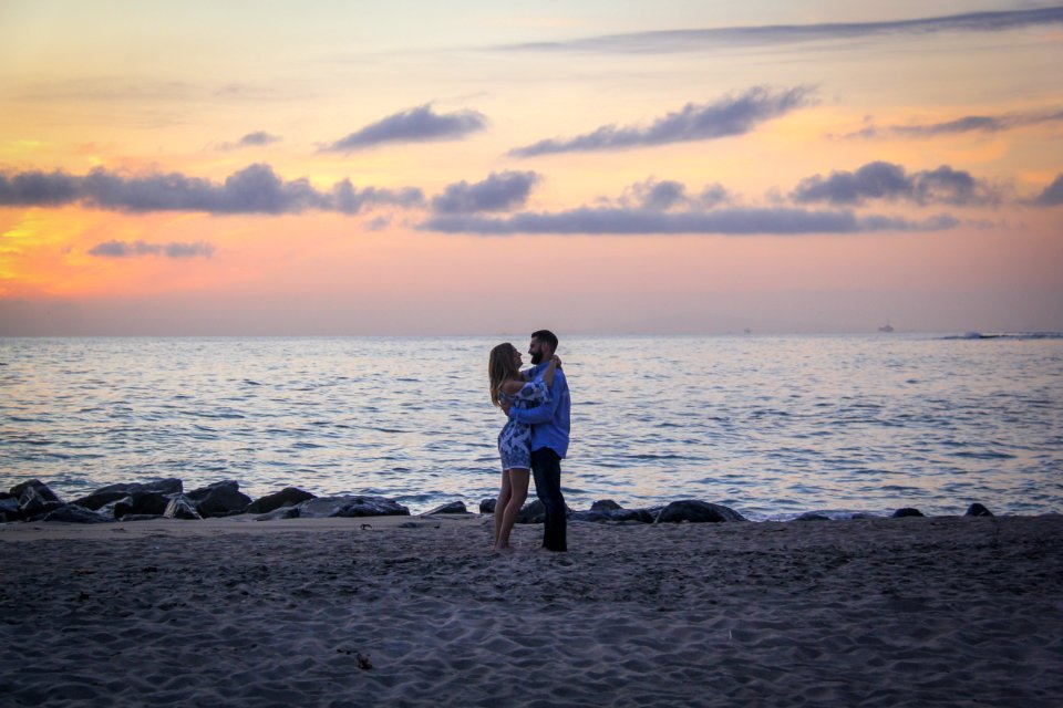 Couple Face To Face Stands On Seashore Near Calm Water During Golden Hour