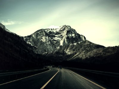 Asphalt Road With Running Vehicle Infront Of Mountain Under Gray Sky