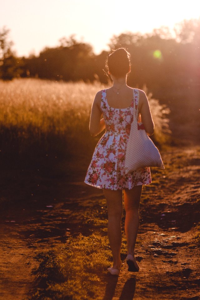 Woman In White And Pink Floral Sleeveless Dress Walking On Brown Road During Sunlight
