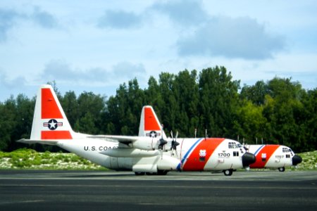 Two U.S. Coast Guard C-130 aircraft parked in front of the NAF Hangar