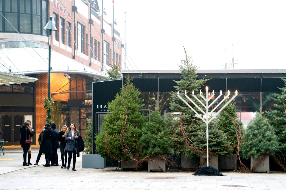 Menorah and people with and without masks in South Street Seaport on an overcast, foggy day.