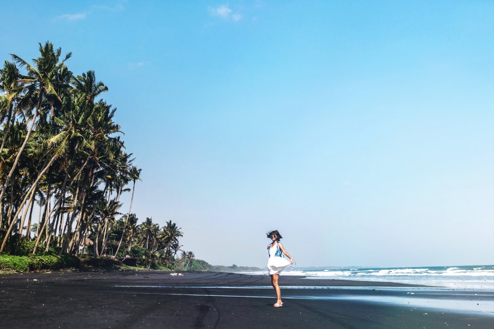 Young woman is spinning on a black sand beach, Bali island.