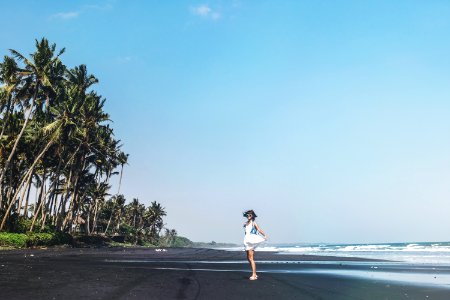 Young woman is spinning on a black sand beach, Bali island. photo