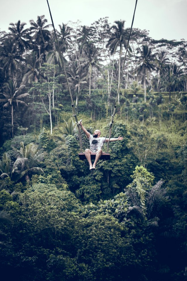 BALI, INDONESIA - DECEMBER 26, 2017: Man having fun on the swing with action camera in the jungle of Bali island, Indonesia. Rainforest, swing.