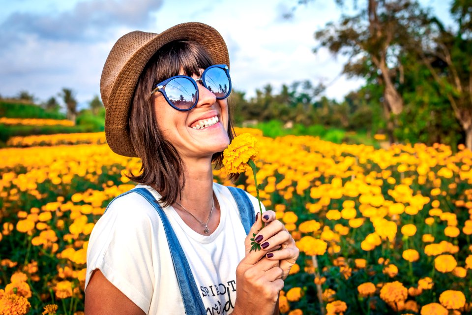 Close up portrait of happy and beautiful young woman relaxing enjoying the fresh beauty of gorgeous orange marigold flowers field in travel and holidays. Bali island.