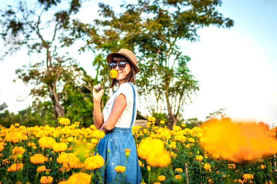 Close up portrait of happy and beautiful young woman relaxing enjoying the fresh beauty of gorgeous orange marigold flowers field in travel and holidays. Bali island.