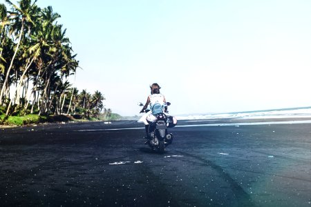 Young woman driving a scooter at the beach with black sand. Bali island. photo