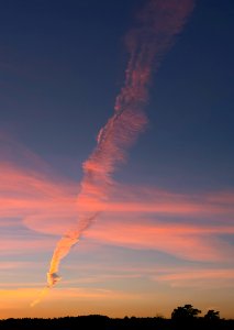 Elongated smoke plume from the oil refinary crossing clouds at sunset 1 photo