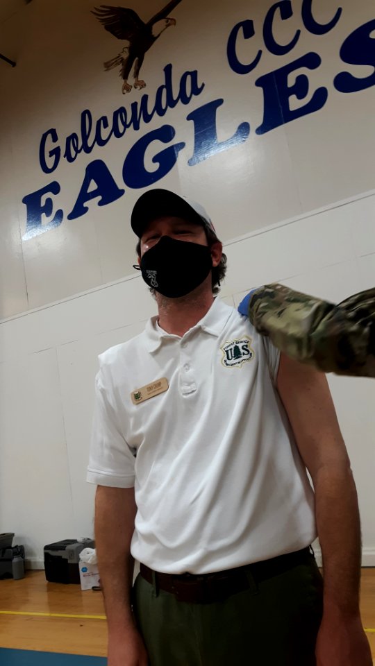 A man wearing a mask during the COVID-19 pandemic receives a vaccination in his upper left arm.