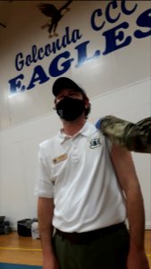 A man wearing a mask during the COVID-19 pandemic receives a vaccination in his upper left arm.