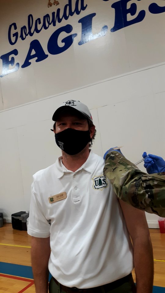 A man wearing a mask during the COVID-19 pandemic receives a vaccination in his upper left arm.