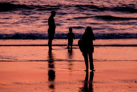 Silhouettes of Parents Taking Photos of Their Son on the Beach at Sunset photo