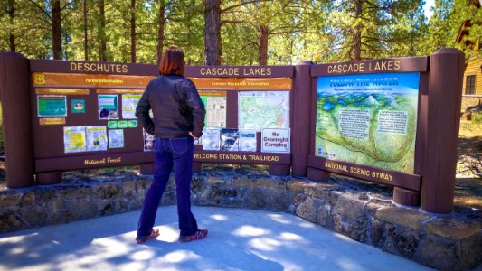 WOMAN READING CASCADE LAKES SIGN-DESCHUTES