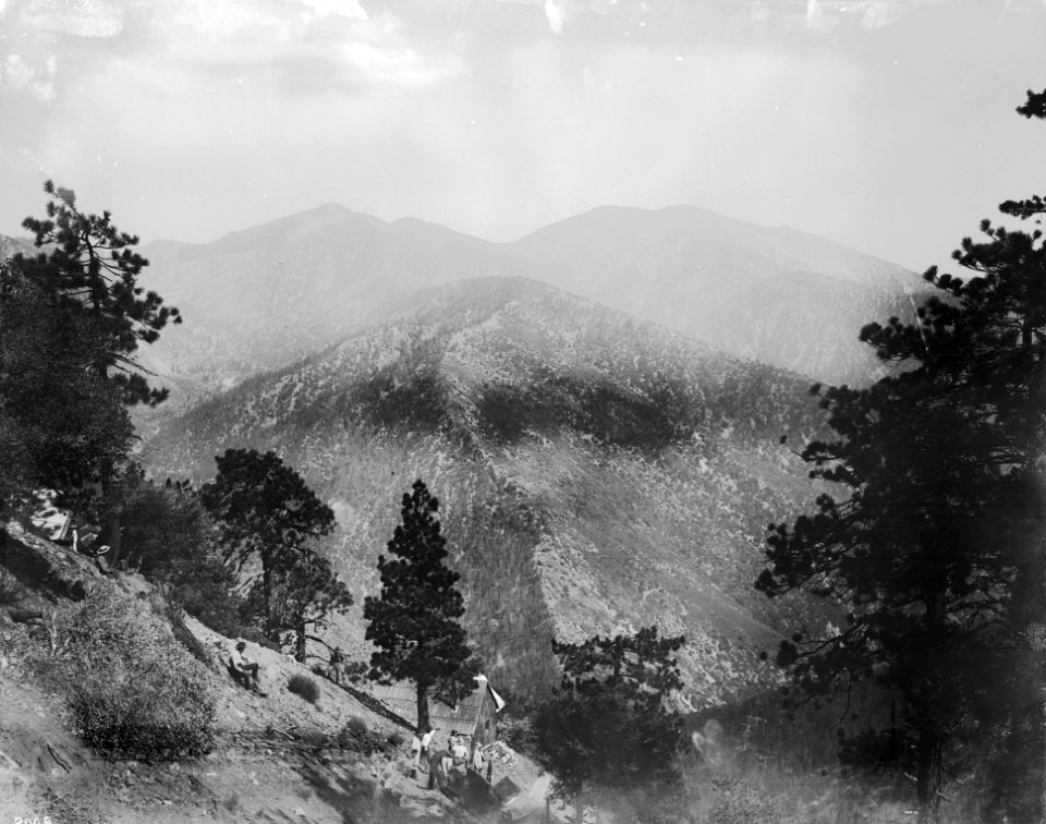 Photograph of a group of about a dozen people on a mountain slope (North Baldy) near a building of the Big Horn Mine looking toward Mount Baldy
