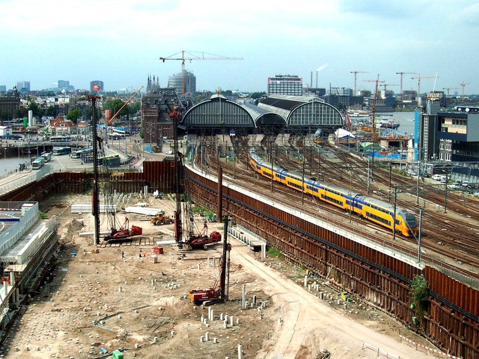 2007.08 - 'Train is leaving the City'- Amsterdam photos, a view over the last excavation of Oosterdok / Docklands area full of ramming on the concrete pilings & the old caps of Central Station; Dutch city + geotag, Arjan Heijnsbroek, The Netherlands