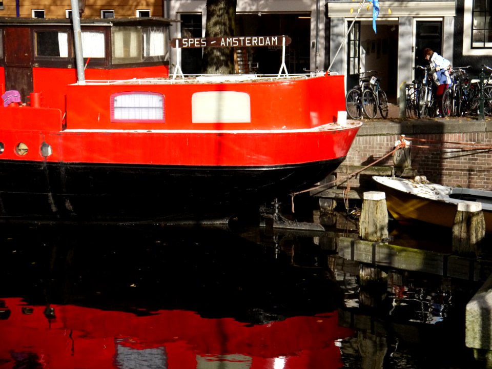A red colored houseboat ship in canal Brouwersgracht near Oranje-bridge - with shadows and reflections in the water;  in Amsterdam, near the corner of Willemstraat, Amsterdam city, November 2013; photo Amsterdam; urban photographer Fons Heijnsbroek, 2013