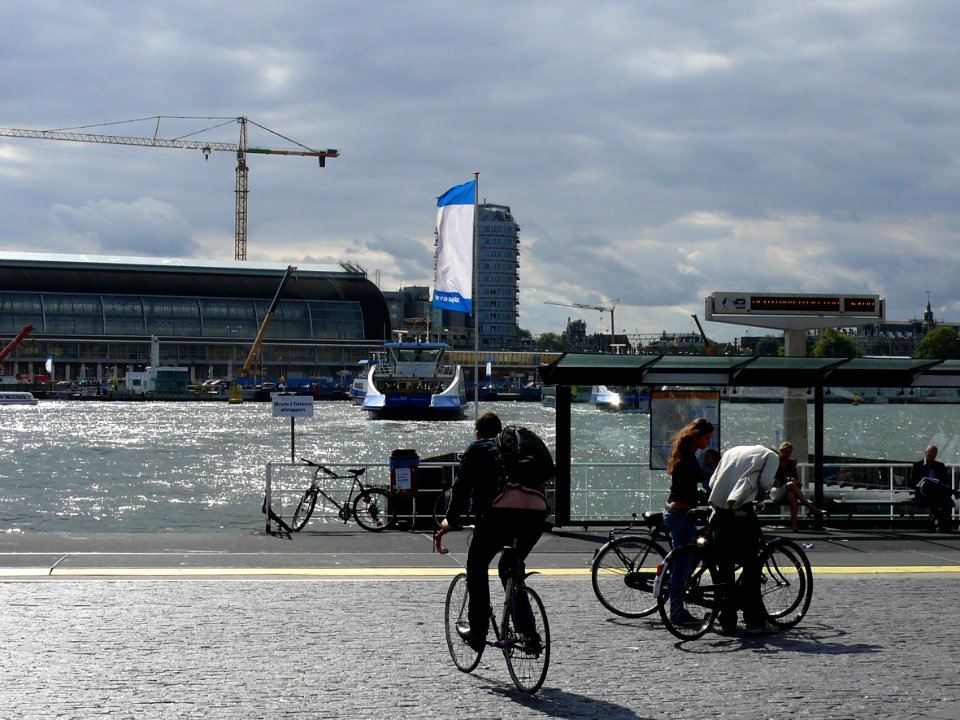 2007.08 - 'Amsterdam cyclists waiting for the ferry' direction Amsterdam Central Station and to the center along the border of river IJ, North side of the city; Dutch urban city photo + geotag, Fons Heijnsbroek, The Netherlands