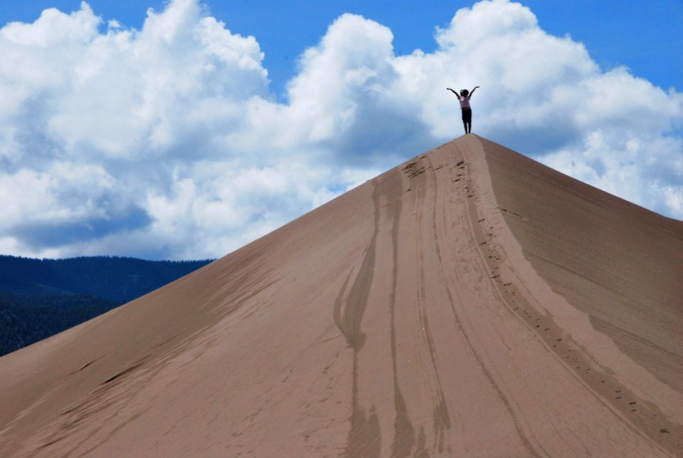 Girl on Dune Summit with Arms Raised Up