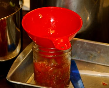 Salsa being added to wide mouth jar for canning