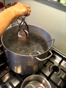 Lowering filled jam jars into boiling water bath canner photo