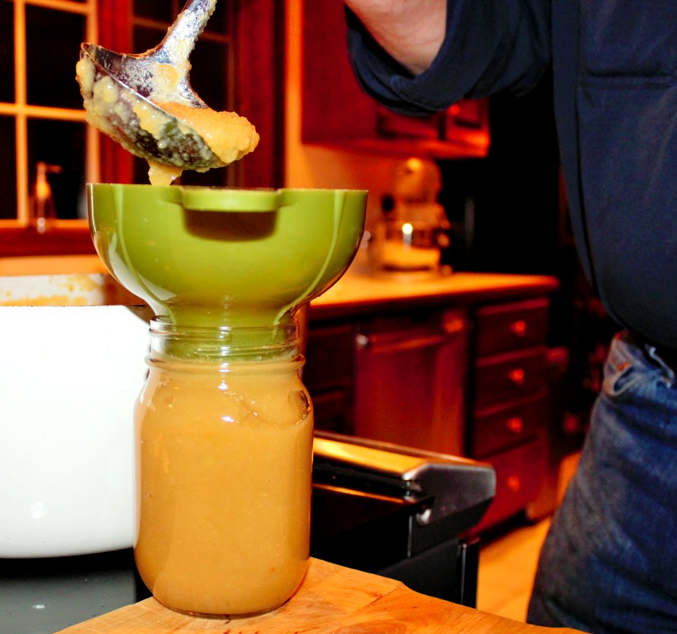 Applesauce being ladled into mason jar