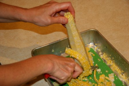 Removing kernels from the cob with knife on cutting board in pan photo
