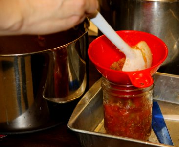 Adding salsa to jar using funnel and ladle photo