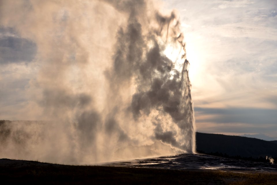 Old Faithful eruption in front of the sun
