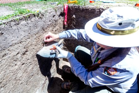 Park Archaeologist Beth Horton pulls an obsidan flake from a dig site photo