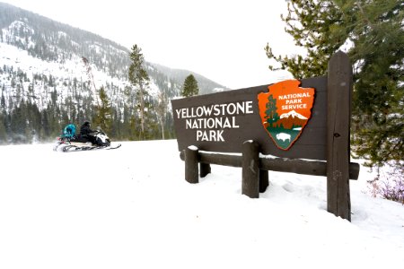 Snowmobiler rides past the Yellowstone National Park East Entrance sign photo