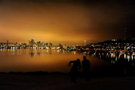 A couple slides down the snowy hill, city lights, Space Needle, view of Queen Anne Hill, Gas Works Park, Lake Union, Wallingford / Fremont, Seattle, Washington, USA