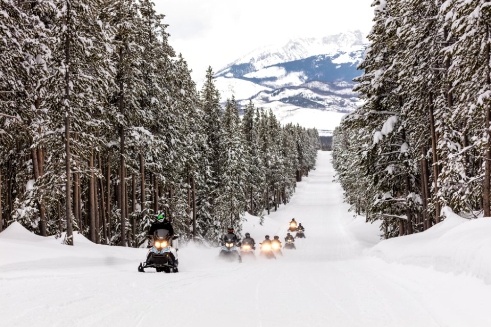 Snowmobiles riding the park road with the Tetons in the background
