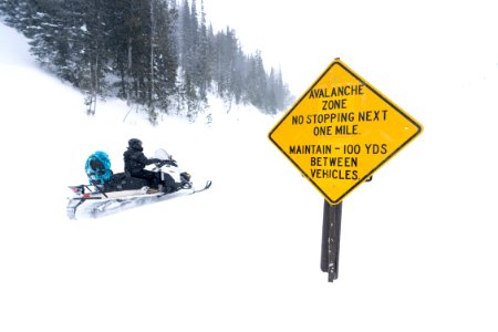 Snowmobiler riding past the avalance zone sign on Sylvan Pass photo