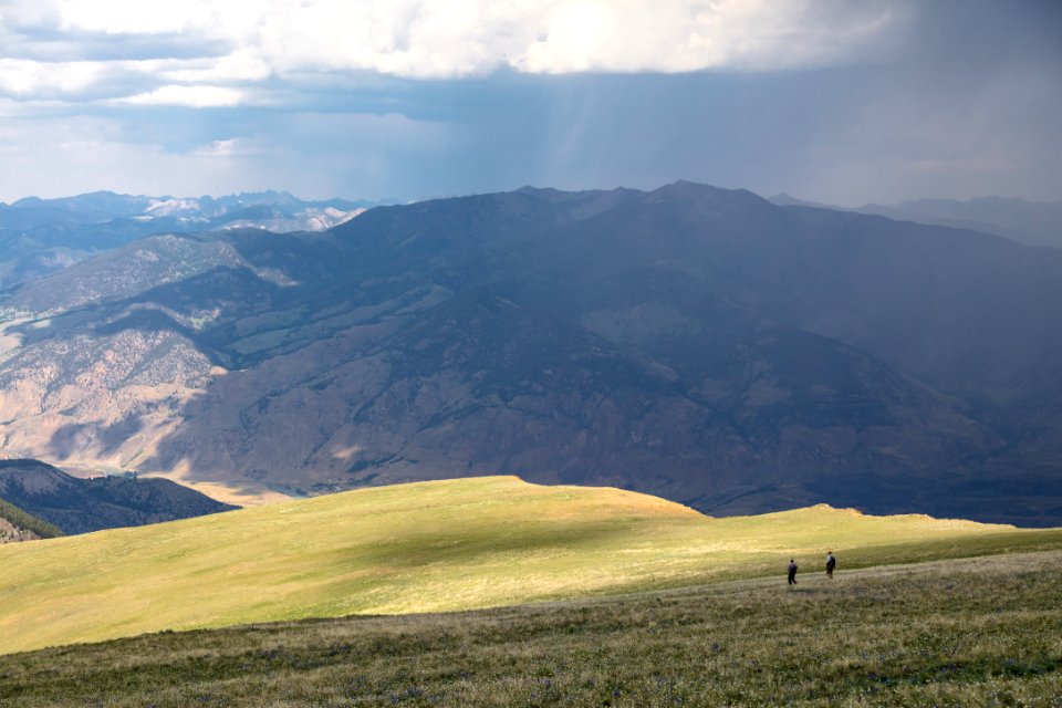 Hikers descending north face of Electric Peak with approaching storm